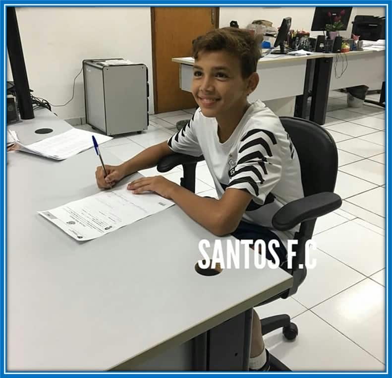 A Dream Realized: A beaming young Deivid captures the moment of triumph, seated with pen in hand, as he signs his first-ever contract with Santos, marking the inception of his professional football journey. Source: Instagram/deividwashington_.