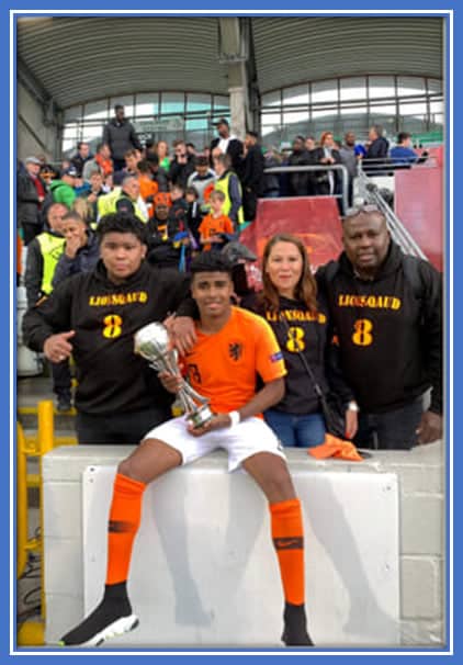 Ian jubilantly raises the U-17 championship trophy, surrounded by the beaming faces of his immediate family members. Credit: FaceBook/wendy.schuitemaker.