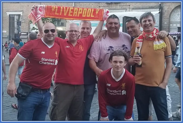 This is a young Harvey Elliott squatting in front of his father, Scott. Their Family were in Kiev to watch the 2018 Champions League final.