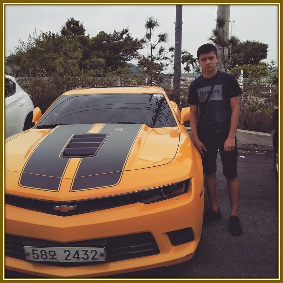 Abdukodir Khusanov striking a pose next to what appears to be his yellow Chevrolet.