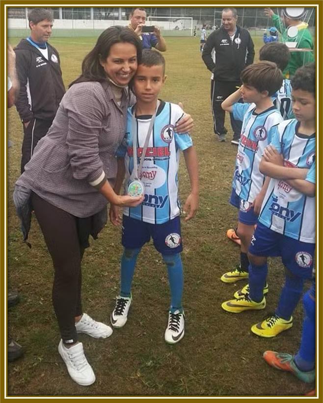 Ana Reis celebrates with her son, Vitor, holding his first big medal. Her face beams with joy and pride, a moment of pure happiness in their journey together.